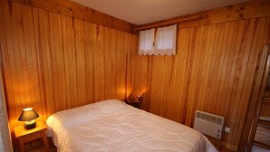Et værelse med træpaneler, en seng med hvid dyne, en sengetavlelampe og en varmekilde.