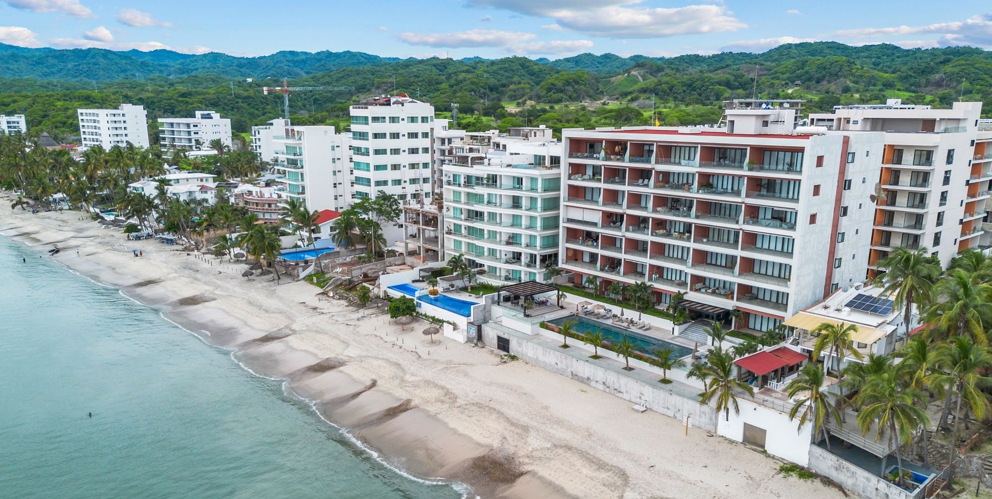 A beachfront hotel with multiple floors, a pool, and a beach view.