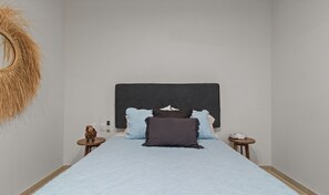 Un dormitorio con cama, mesita de noche, espejo instalado en la pared y teléfono fijo en la pared.