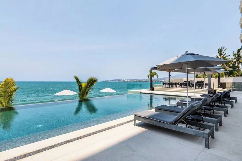 Un espace aménagé au bord de la piscine, avec des chaises longues et des parasols, donnant sur une étendue d’eau.