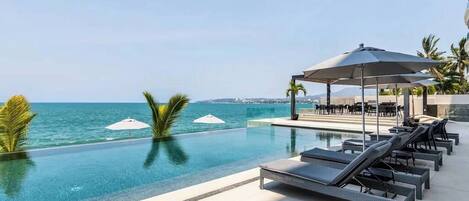 Un espace aménagé au bord de la piscine, avec des chaises longues et des parasols, donnant sur une étendue d’eau.