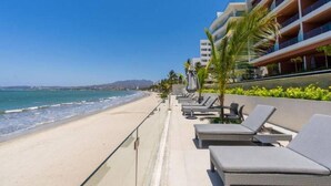 Et hotel ved stranden med poolområde, liggestole og havudsigt.