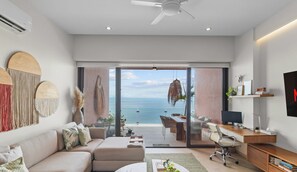 A modern living room with a large sliding glass door leading to a balcony with a view of the sea.