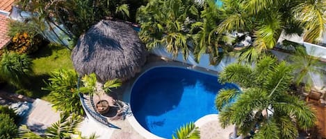 Vista aérea de um resort com uma piscina central rodeada por vegetação exuberante e palmeiras.