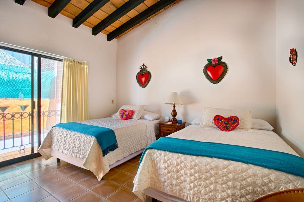 Habitación de hotel con dos camas, un balcón y decoración con forma de corazón en la pared.