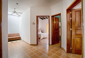 A hallway with a tiled floor, a ceiling fan, a wooden door, and a bed in the adjacent room. - Villa Delfin: Golden Zone 3BR with Private Pool (Bucerias)
