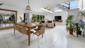 A spacious living area with a wooden dining table, wicker chairs, and a large mirror.