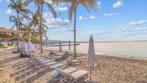 A beach with sun loungers, umbrellas, and palm trees.