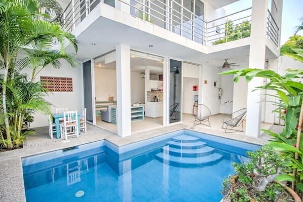 Un moderno edificio de dos pisos con piscina, mobiliario exterior y balcón.