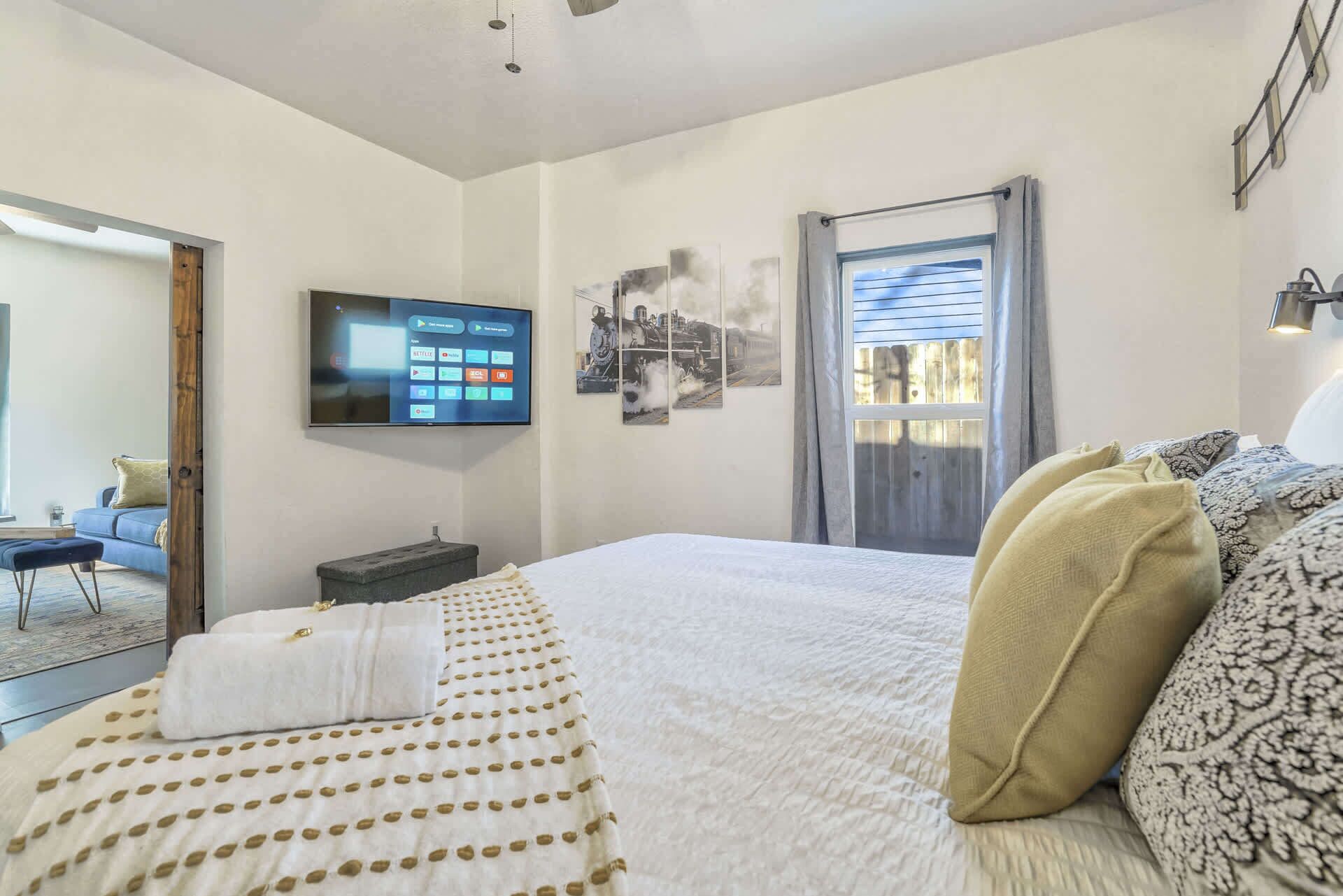 A bedroom with a bed, a TV mounted on the wall, and a window with curtains.