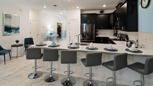Uma cozinha moderna com armários escuros, uma ilha central com banquetas e uma área de jantar com mesa e cadeiras.