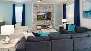 Uma sala de estar moderna com uma TV de tela plana fixada em uma parede de pedra, um sofá cinza, uma poltrona branca e uma mesa de centro com uma planta.
