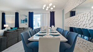 Uma sala de jantar moderna com uma mesa comprida posta para refeição, cadeiras azuis e um lustre contemporâneo.