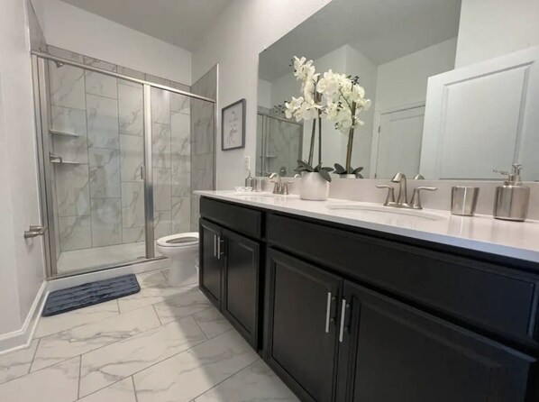 A modern bathroom with a walk-in shower, a toilet, a large mirror, and a vanity with a sink and two bottles of soap. - Amazing Modern Home 10BR/ 5BH - Pool/Spa/Game Room (Kissimmee)