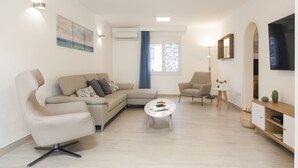 Un salon moderne comprenant un canapé, un fauteuil, une table basse et un téléviseur à écran plat.