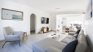 Un salon moderne avec un canapé, un fauteuil, un téléviseur et, au fond, un coin repas.