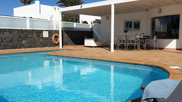 Une piscine bordée d’un muret en pierre et une terrasse couverte aménagée avec du mobilier d’extérieur.
