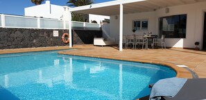 A swimming pool with a stone wall and a covered patio area with outdoor furniture. - Villa Apollo/Aphrodite (Puerto del Carmen)