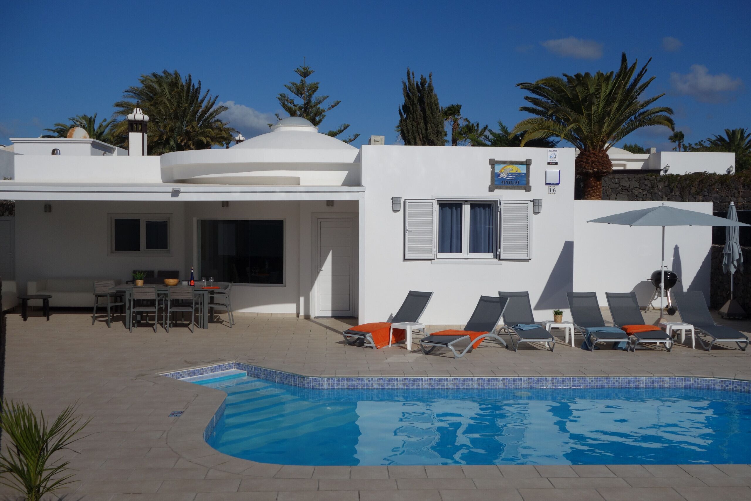 Una villa moderna con piscina, mobiliario exterior y palmeras.