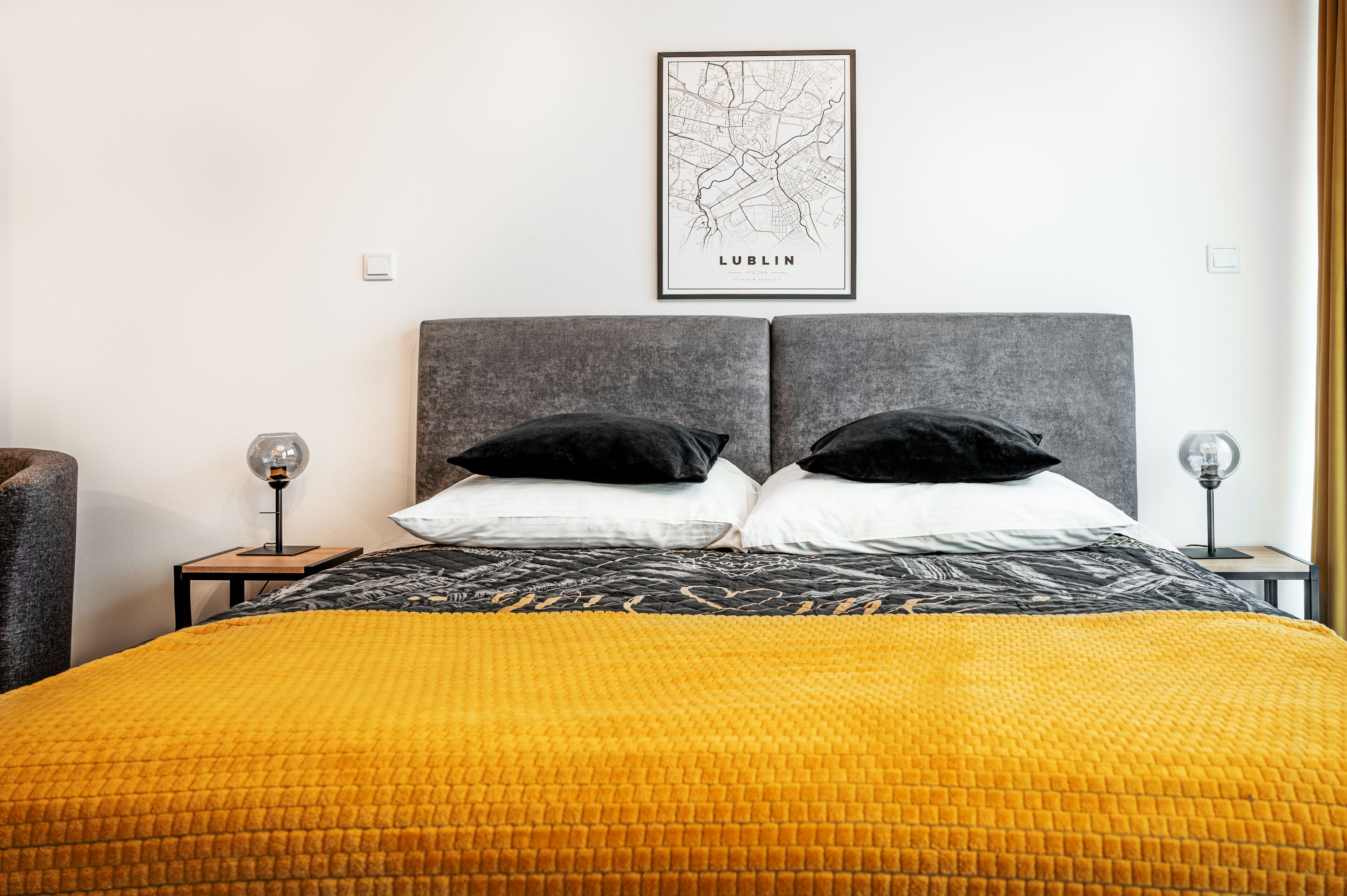 Habitación de hotel con una cama grande, dos almohadas negras, una colcha amarilla con textura, un mapa enmarcado de Dublín en la pared y dos lámparas de noche.
