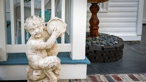 A stone statue of a child holding a drum, placed on a white bench with a blue top, in front of a white door with a window.