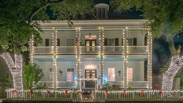 A two-story building with a balcony, surrounded by a white picket fence, and decorated with string lights.