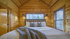 A wooden cabin bedroom with a bed, a window, and a door. - 5Kings | Pool Table, Shuffleboard, Playset, Putt Putt | 2min to New Casino! (Broken Bow)