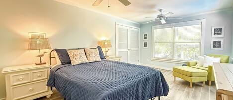 A bedroom with a bed, bedside tables, a desk, a chair, a ceiling fan, and a window with blinds.