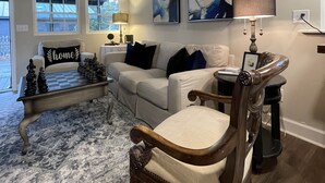 Una sala de estar con una mesa de centro a cuadros, un sofá, una silla de madera y dos cuadros colgados en la pared.