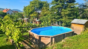 Une piscine en bois avec un escalier, entourée de verdure et bordée d’une structure en bois.