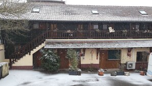 Un bâtiment traditionnel à deux étages, doté d’un toit en tuiles, d’un escalier en bois et de plantes en pot au premier plan.