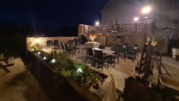 Un espace extérieur aménagé en terrasse avec des tables et des chaises, un petit jardin avec des plantes et un bâtiment en arrière-plan.