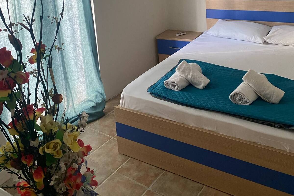 Habitación de hotel con cama, mesita de noche, aire acondicionado de pared, un cuadro y ventana con cortina.