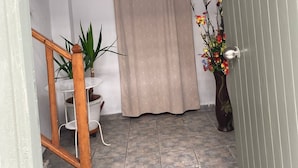 A hallway with a wooden staircase, a beige curtain, a potted plant, and a vase with flowers. - Nostalgia (Skiathos)