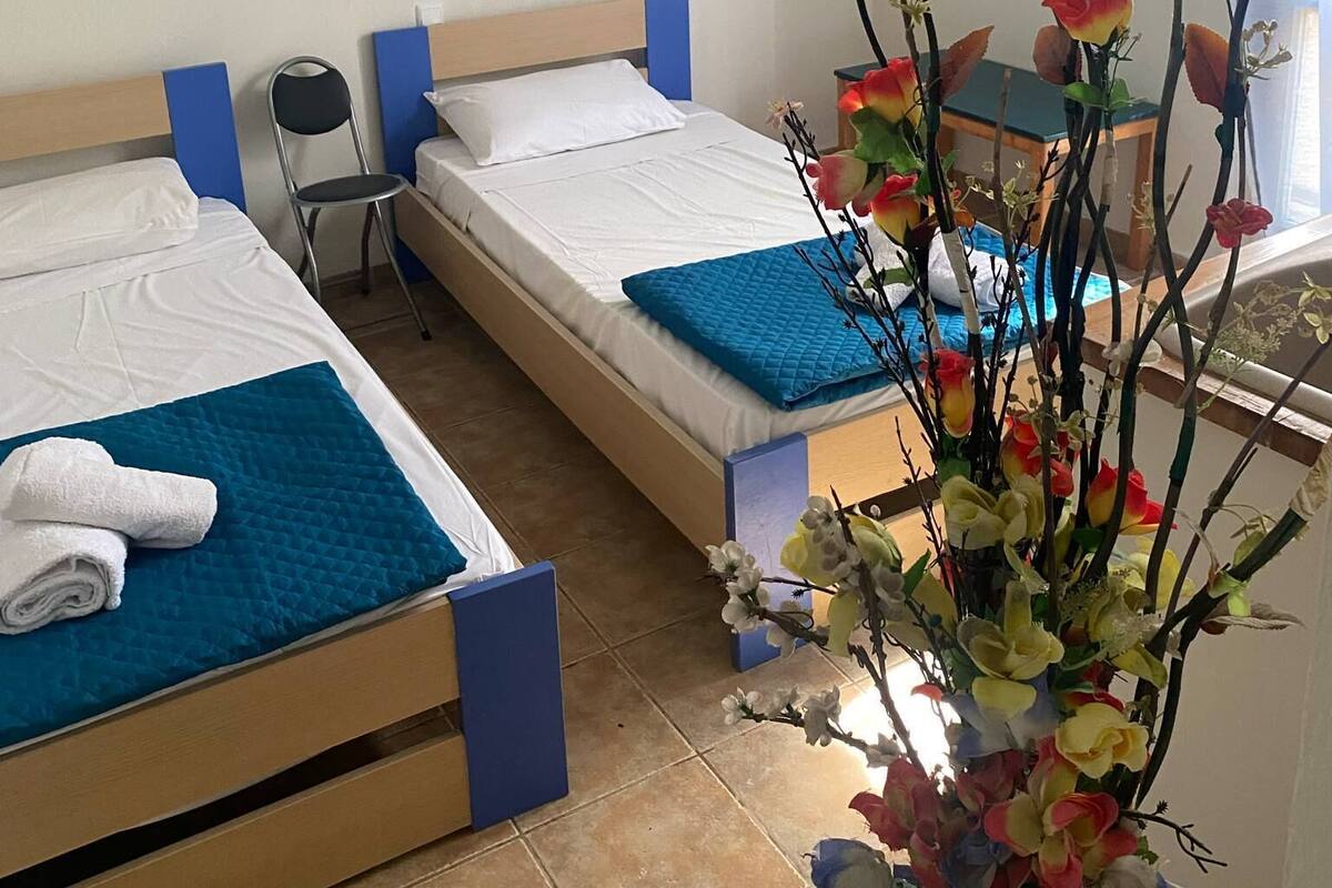 Habitación de hotel con dos camas individuales, una mesita, una silla, un florero y un cartel en la pared.