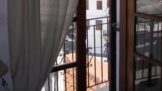 A room with a view of a hillside through a window with a curtain. - Nostalgia (Skiathos)