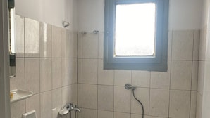 A bathroom with a toilet, a sink, a shower, and a window. - Nostalgia (Skiathos)