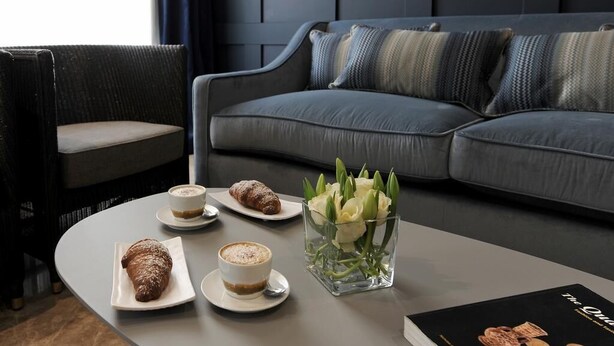 A modern living room with a grey sofa, a round coffee table, and a chair. There are pastries and a coffee cup on the table. - The Manoel Hotel (Valletta)