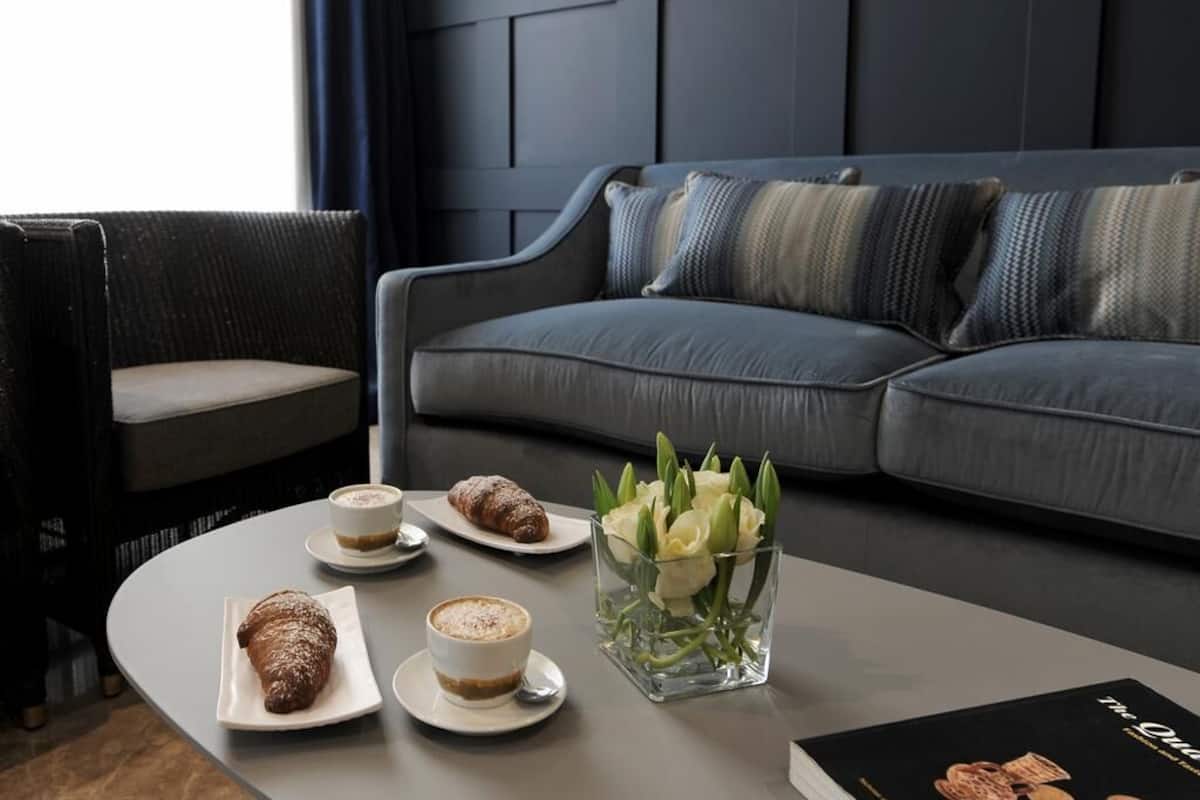 Ein modernes Wohnzimmer mit einem grauen Sofa, einem runden Couchtisch und einem Sessel. Auf dem Tisch befinden sich Gebäck und eine Kaffeetasse.