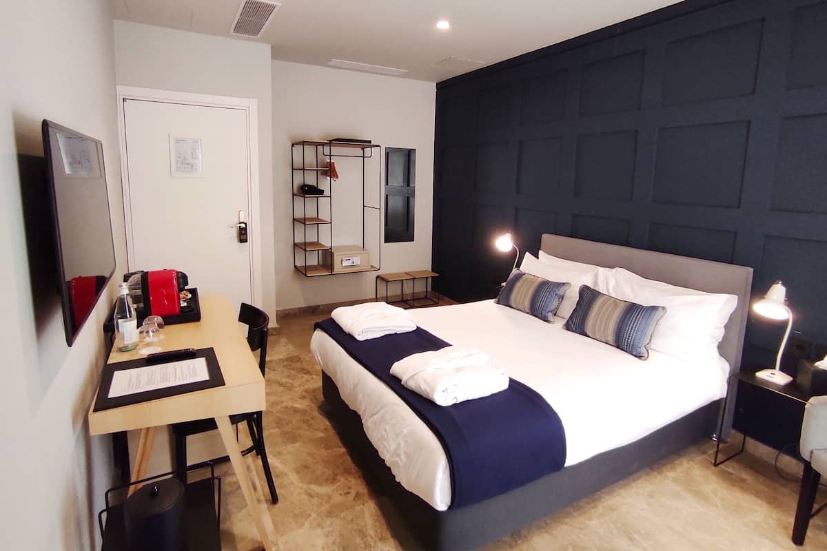 Ein modernes Hotelzimmer mit einem großen Bett, einem Schreibtisch mit Computer, einem Stuhl, einem Kleiderschrank und einem Fernseher.