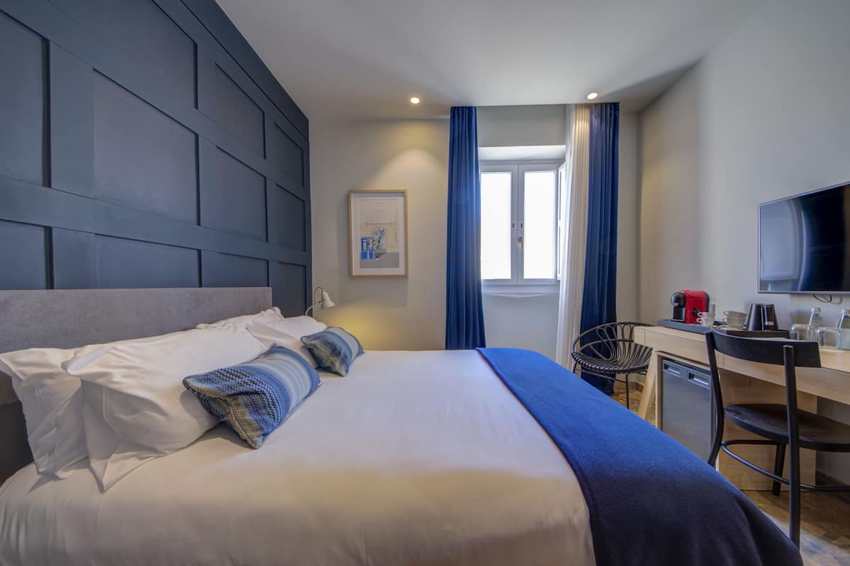 Ein Hotelzimmer mit einem großen Bett, einem Schreibtisch mit Stuhl, einem Fernseher und einem Fenster mit Vorhängen.