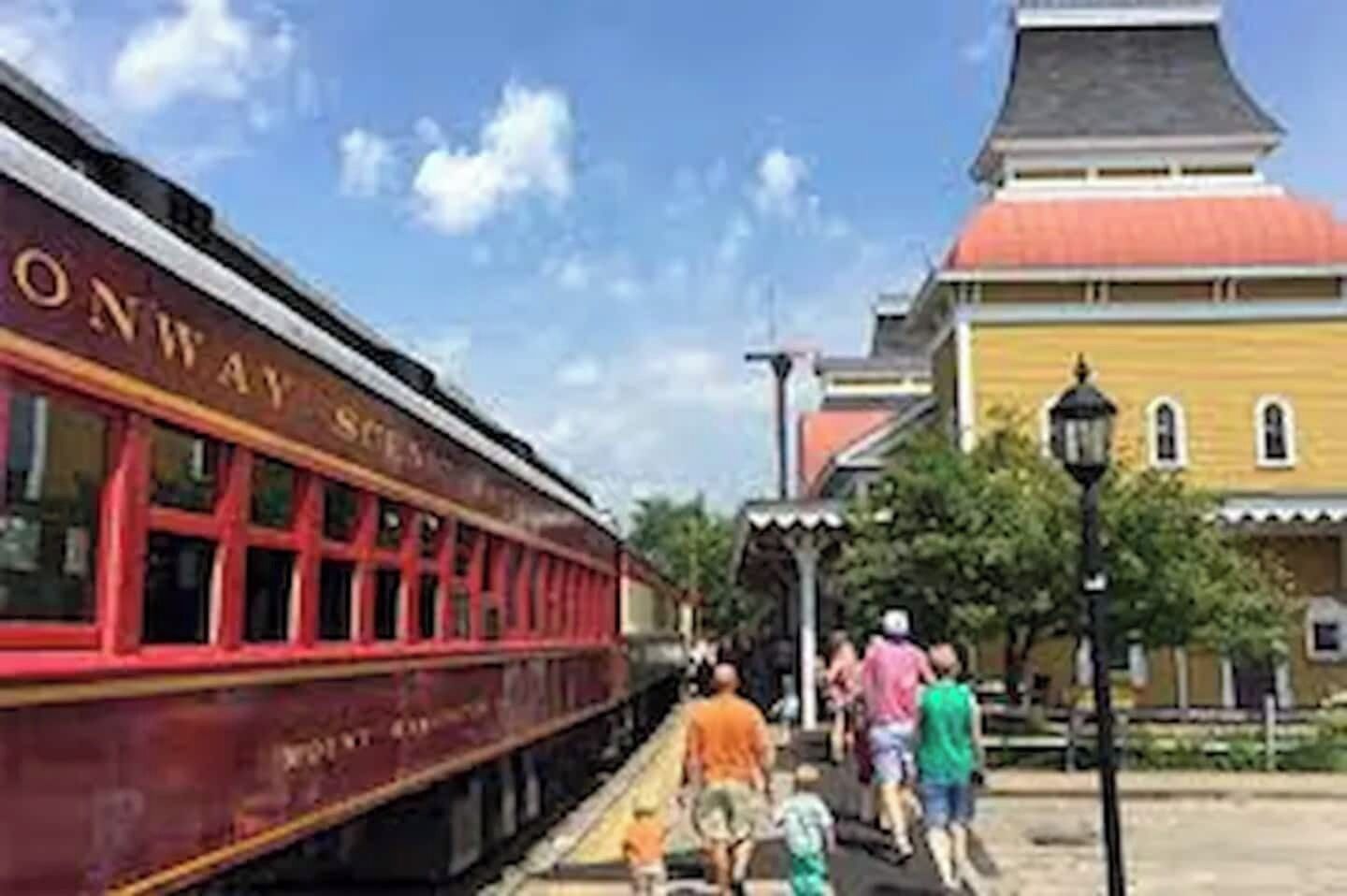 Une gare avec un train rouge portant l’inscription « ONWAY SCENES » et un bâtiment jaune avec un toit rouge.
