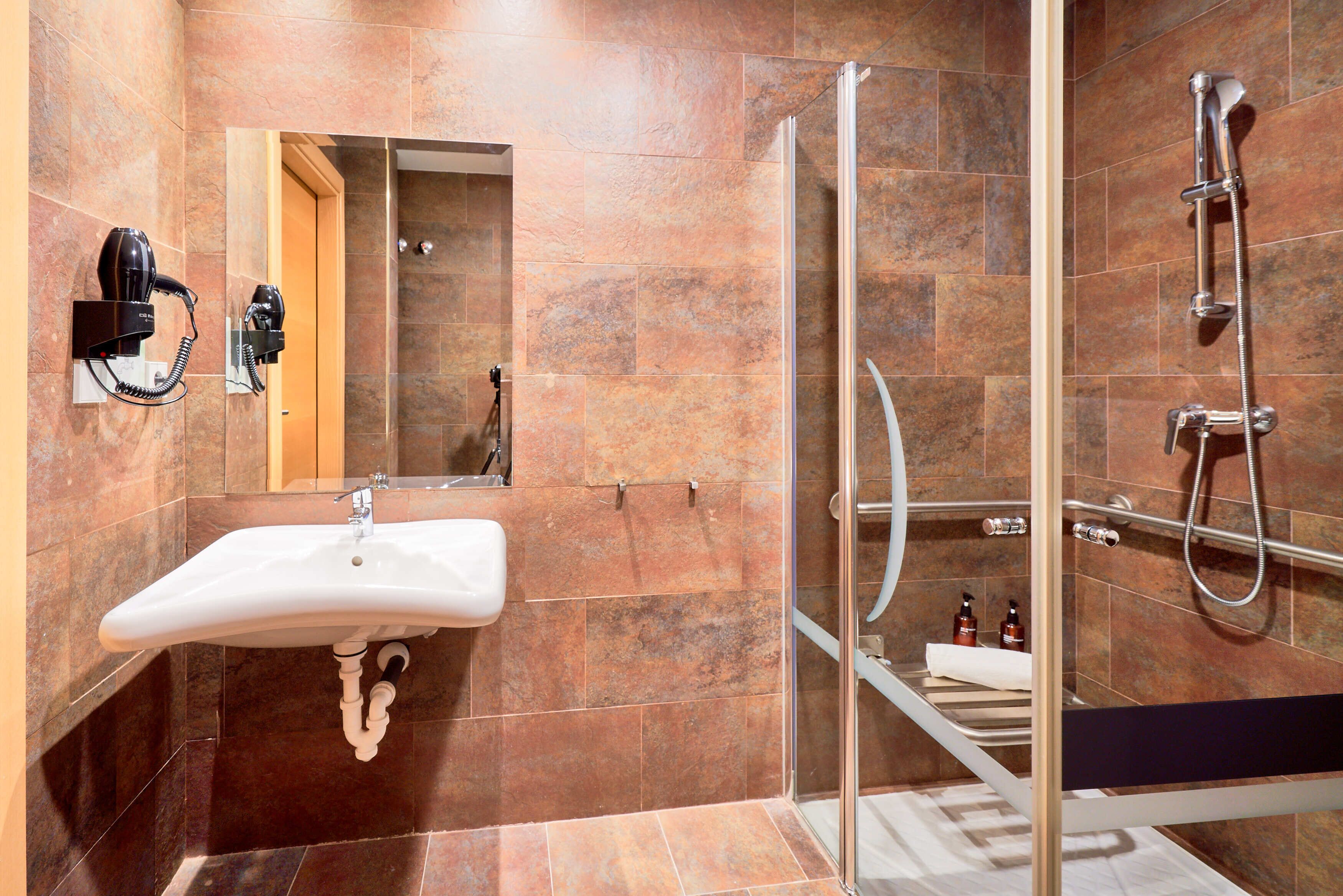 A modern bathroom with a glass shower enclosure, a sink with a towel rack, and a hairdryer mounted on the wall.