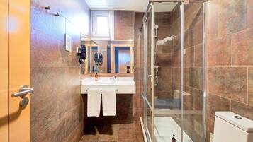 Un baño con cabina de ducha de vidrio, un lavamanos con toalla y un inodoro.