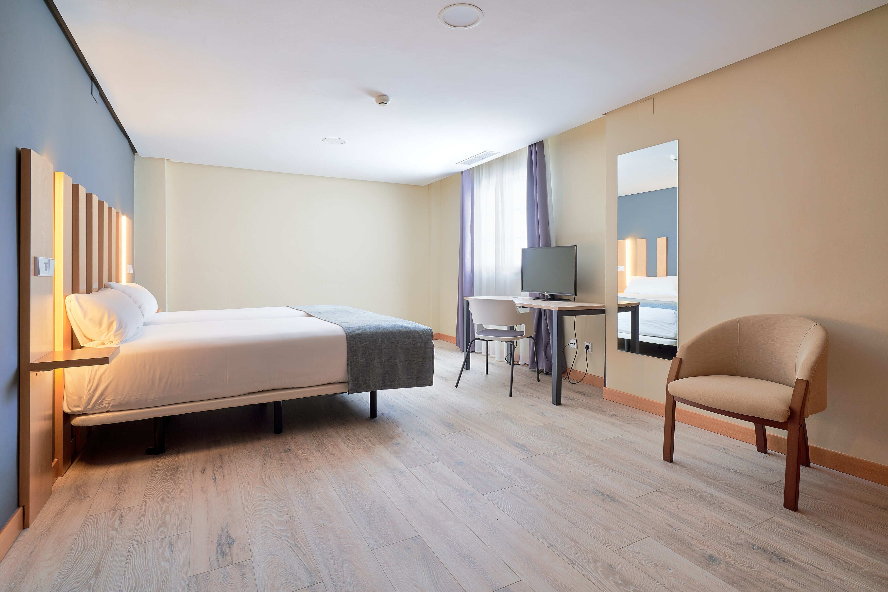 Una habitación de hotel con una cama, un escritorio, una silla y un televisor.