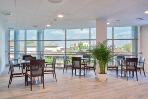 Amplio espacio interior con ventanas grandes, suelo de madera y varias mesas y sillas dispuestas para comer o reuniones.