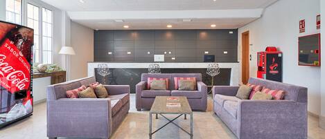 A modern hotel lobby with three sofas, a coffee table, and a large flat-screen TV.