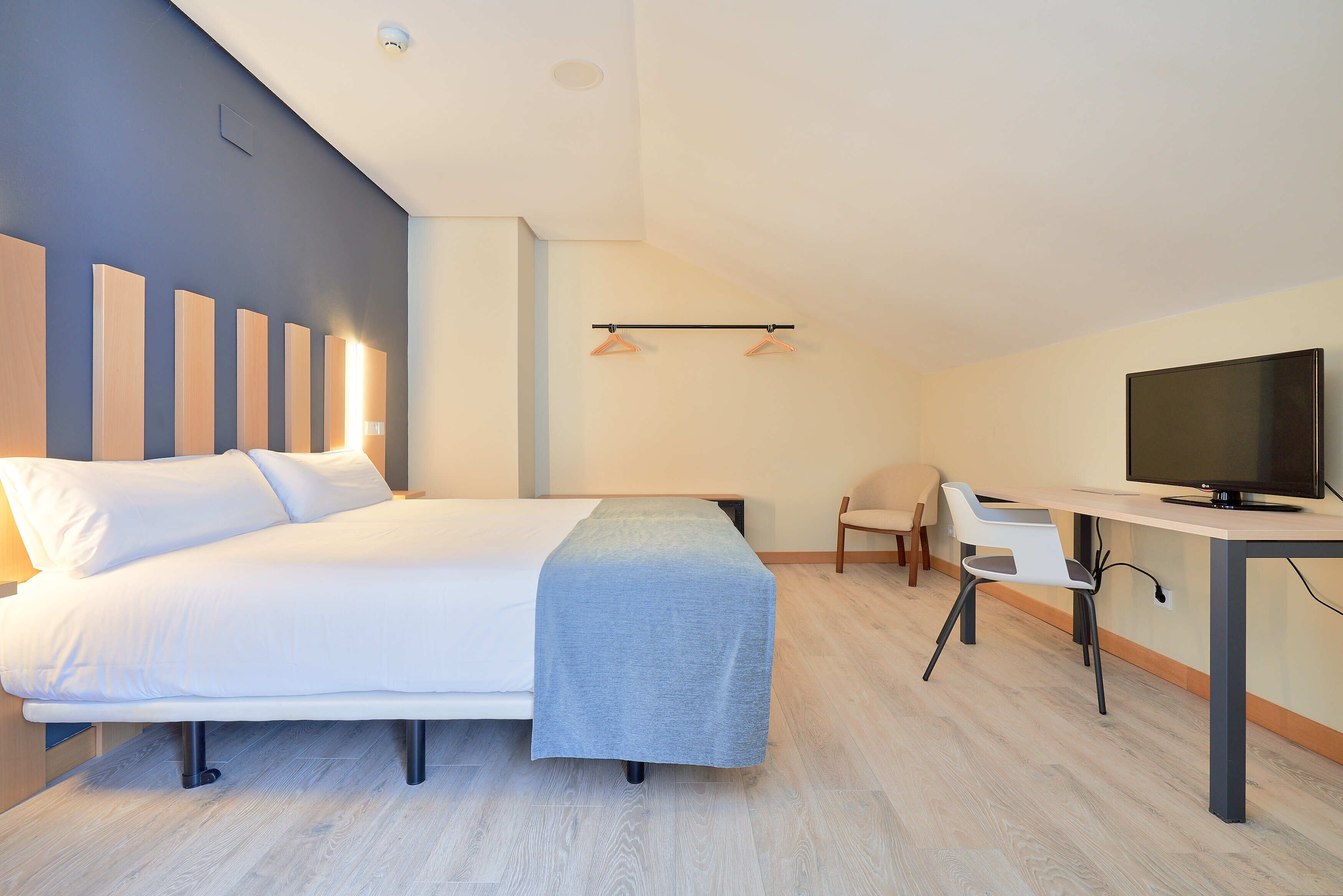 A modern hotel room with a bed, a desk with a TV, and a chair.