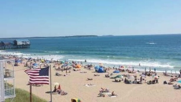 A beach with people, a pier, and an American flag.