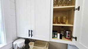 A kitchen with white cabinets, a dish rack, and various kitchen items.